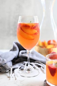 two glasses filled with liquid and fruit next to each other on a white counter top