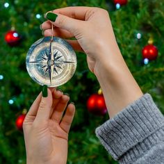 a person holding up a compass in front of a christmas tree with ornaments on it