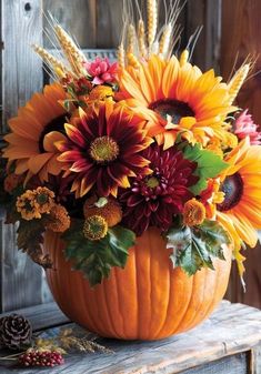 a pumpkin filled with lots of flowers sitting on top of a wooden table next to a pine cone