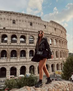 a woman standing on top of a stone wall next to an old roman collise