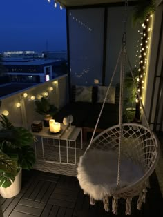 a white hanging chair on top of a balcony next to potted plants and candles