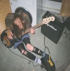 a person sitting on the ground with a guitar in their lap and headphones to their ears