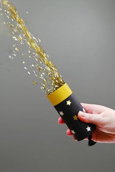 a hand is holding a black and gold paper tube with stars coming out of it