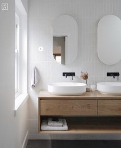 two white sinks sitting on top of a wooden counter in a bathroom next to mirrors