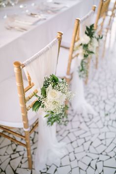 the chairs are lined up with white flowers and greenery