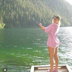 a woman standing on a dock holding a fishing rod in her hand and looking at the water