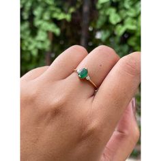 a person's hand holding a ring with a green stone on it and trees in the background