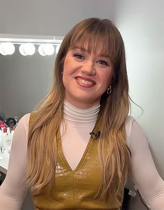 a woman with long blonde hair is smiling at the camera while standing in front of a mirror