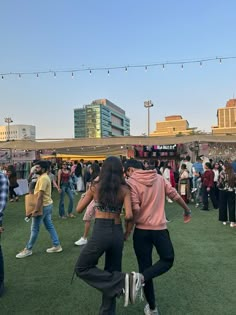 two people dancing in the middle of an open field with string lights strung above them