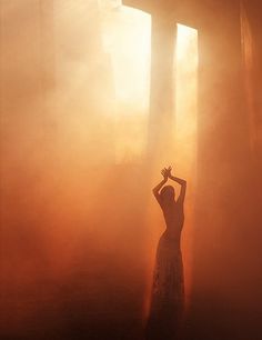 a woman standing in the middle of a foggy forest with her arms raised up