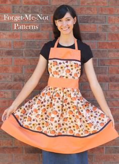 a woman standing in front of a brick wall wearing an orange apron and black shirt