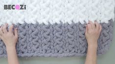 two hands are on the edge of a blanket that has been knitted with yarn