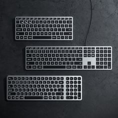 three computer keyboards sitting next to each other on top of a black surface with wires