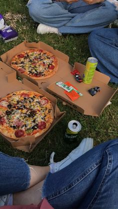 three pizzas sitting on the grass with people eating them and drinking soda bottles next to them