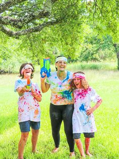 two girls and an older woman standing in the grass with paint splattered on them