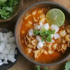 two bowls filled with food on top of a wooden table next to rice and cilantro