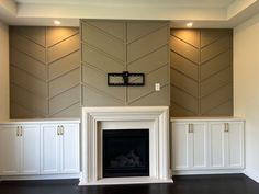 an empty room with white cabinets and a fireplace in the center is decorated with chevron wallpaper