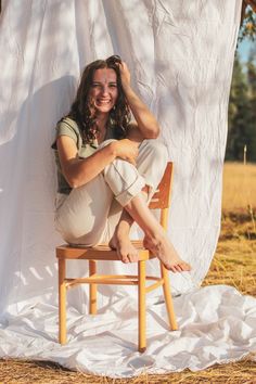 a woman sitting on top of a wooden chair in front of a white sheet covered wall