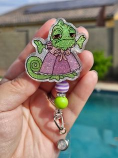 a hand holding a keychain with a green and purple frog on it's side