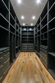 an empty walk - in closet with wooden floors and black shelving unit doors, lights on the ceiling