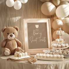 a teddy bear sitting on top of a table next to a sign and desserts