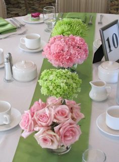 the table is set with pink and green flowers in vases on top of it