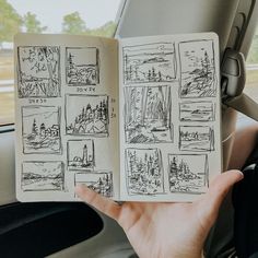 a hand holding an open book in front of a car window with drawings on it