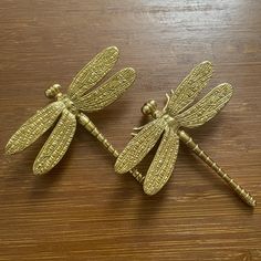 two brass dragonflys sitting on top of a wooden table