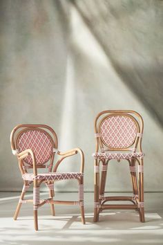 two wicker chairs sitting next to each other in front of a wall with light coming through it