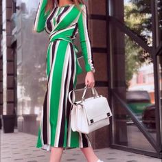 a woman in a green and black striped dress is holding a white handbag while walking down the street