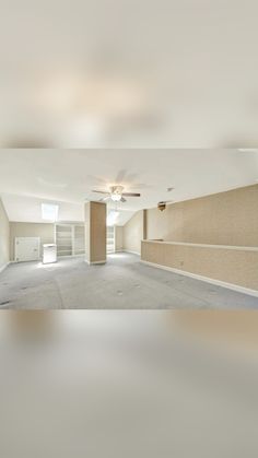 an empty living room with no furniture and ceiling fan in the center, is seen from across the room