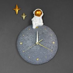 a clock with an astronaut sitting on top of it next to two gold star decorations