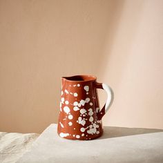 a brown and white pitcher sitting on top of a table next to a pink wall