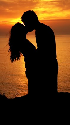 a couple kissing in front of the ocean at sunset