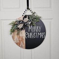 a christmas wreath hanging on the front door with merry christmas written in white and black