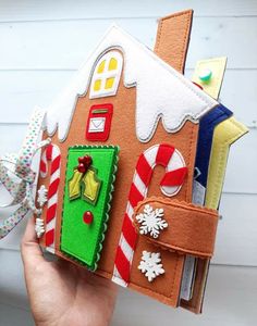 a hand holding a small felt house with candy canes and decorations on the outside