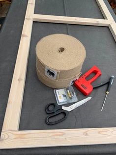 a roll of brown paper next to scissors and tape on top of a wooden frame