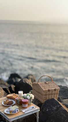 a picnic table with food on it next to the water and rocks by the ocean