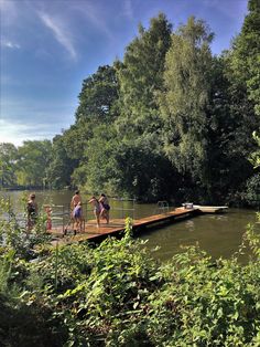 people are standing on a dock in the middle of a body of water near some trees