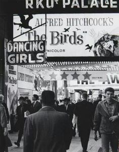 black and white photograph of people walking in front of a theater sign that reads rkot palace