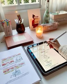 a person sitting at a table with a tablet and pen in their hand, next to some books