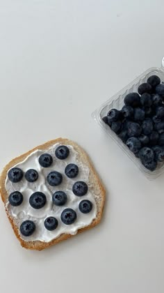 a piece of bread with blueberries on it next to a container of yogurt