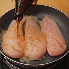 someone pouring sauce on raw chicken in a frying pan