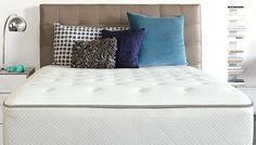 a bed with lots of pillows on top of it next to a night stand and lamp