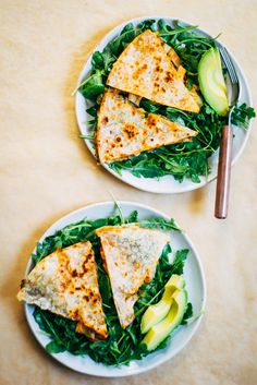 two plates with quesadillas and avocado on them sitting on a table