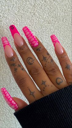 a person with pink nails and tattoos on their fingers, holding up her hand in front of the camera