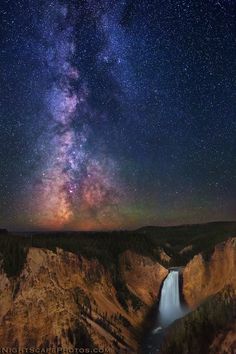 the night sky is filled with stars above a canyon and waterfall in yellowstone national park