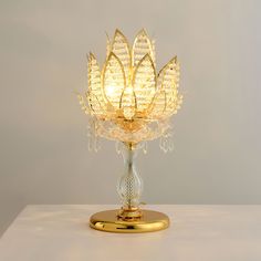 Inspired by the elegance and purity of the lotus, its golden borders combined with delicate crystal leaves resemble a blooming lotus, emitting brilliant light. Light Source Requires three 5-watt maximum (G9) bulbs. (Not included bulbs) Dimmable with compatible dimming bulbs. Measurements Diameter: 11.8" Fixture Height: 18.9" Base diameter: 7.9" Plug Cord On/Off Switch: 59" Features Material: Metal, Crystal. Finishes: Gold. UL listed , CE, SAA, SASO etc. Manufacturer Resources Specification Sheet Ashley Bedroom, Crystal Chandelier Kitchen, Hallway Wall Lights, Tiffany Style Table Lamps, Tiffany Table Lamps, Chandelier Art, Blooming Lotus, Kitchen Island Chandelier, Recessed Wall Lights