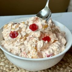 a white bowl filled with fruit salad on top of a woven place mat next to a metal spoon