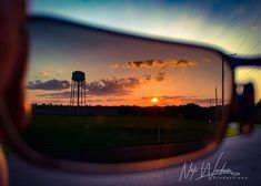 the sun is setting in front of a water tower with clouds reflected in it's rear view mirror